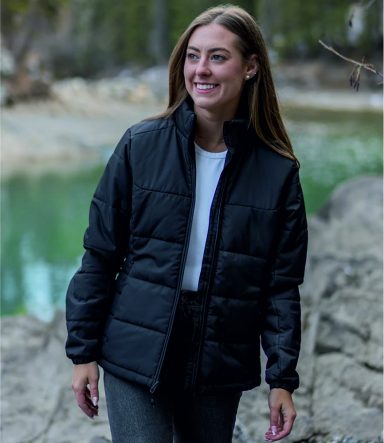 Smiling woman wearing a black quilted jacket by a riverbank.