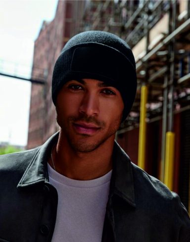 Young man wearing a black beanie and grey jacket, standing in an urban environment.